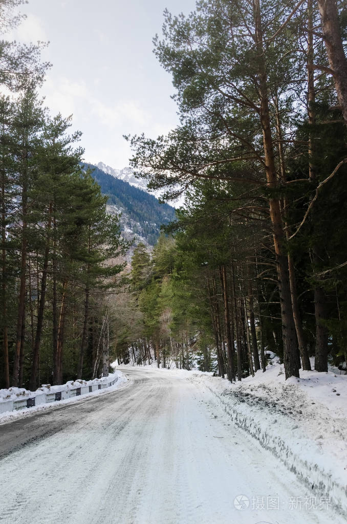 一条在松树林中覆盖着积雪和沙子的冬日山路的景色雪下的沥青路季节和