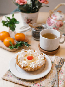 在木桌上配有茶具橘子和 fkowers 的奶油果挞的特写视图