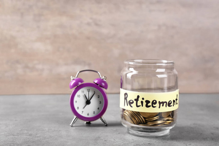 在玻璃瓶中的硬币, 标签 退休 和闹钟在桌子上。养老金计划