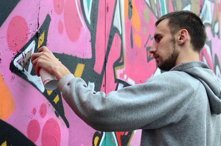 一个穿着灰色帽衫的年轻人在雨天的墙上画上了粉红色和绿色的涂鸦。