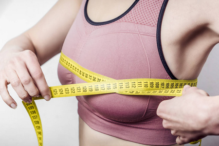 饮食观念, 减肥。特写的年轻女子测量她的乳房用卷尺