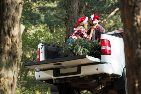 低角度的情侣在圣诞老人的帽子亲吻在树干与圣诞树在森林里