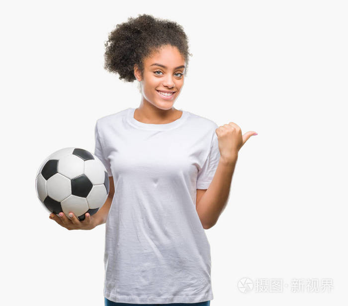 年轻美丽的美国黑人举行足球足球在孤立的背景指向和显示与拇指的一面微笑着快乐的脸