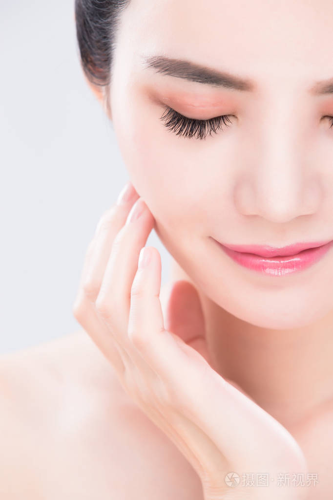 女人闭着眼睛抚摸着脸在灰色的背景下美容护肤的概念