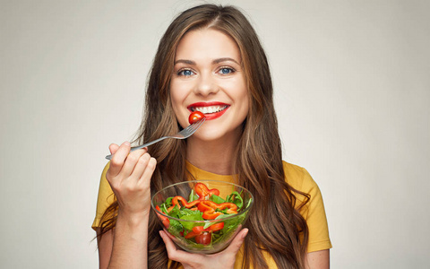 微笑的妇女吃蔬菜沙拉用叉子