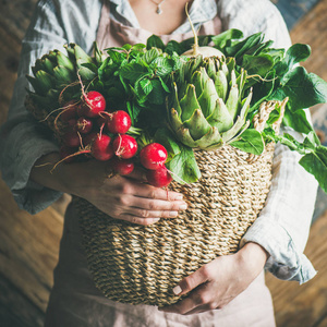 女农夫穿着粉彩亚麻围裙和衬衣持有篮子新鲜季节性蔬菜在她的手