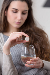 不健康的生病的妇女服用药片与玻璃水