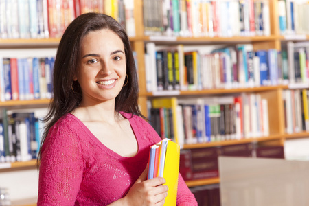 快乐的女学生在图书馆拿着书