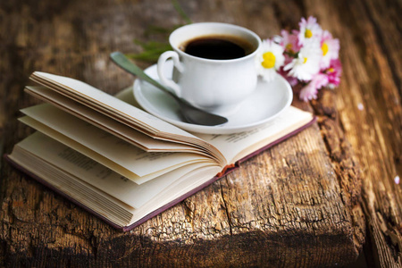 咖啡和纸床单咖啡杯的特写镜头与鲜花和书在木桌上照片