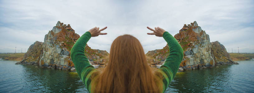 红头发的女孩穿着绿色的毛衣站在山前的山边和举手。概念理念的自由, 梦想, 冥想, 动力。女孩与胜利标志