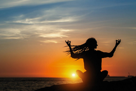 瑜伽剪影冥想的女孩在海洋中的惊人的日落