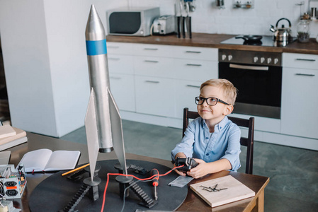 可爱的男孩坐在桌子和测试火箭模型在厨房上周末