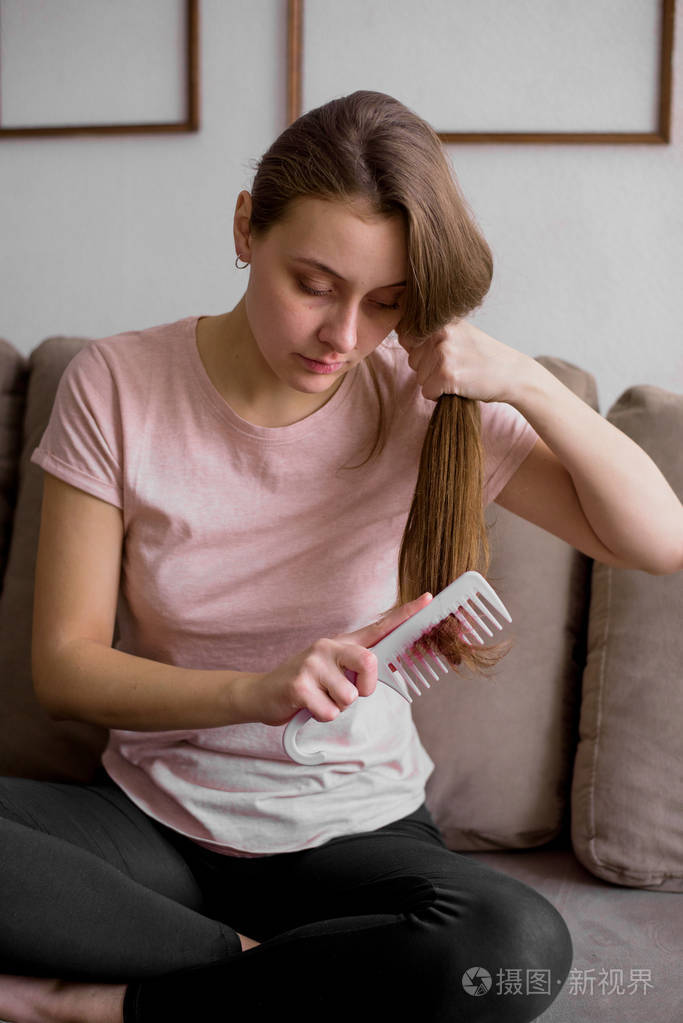 坐在沙发上的有吸引力的年轻妇女的画像在家, 梳一个人的头发
