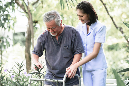 护士与病人使用沃克在退休回家。年轻的女护士手持老人的手在户外花园散步。高级护理护理人员和高级退休家庭服务概念