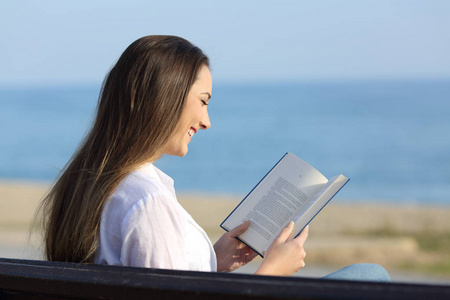 在沙滩上坐在长凳上看书的女人