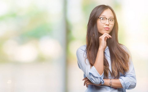 年轻的亚洲商界女性戴着眼镜, 在孤立的背景下, 手放在下巴思考问题, 沉思的表情。微笑与周到的脸。怀疑概念