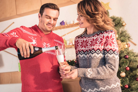 幸福夫妇在圣诞毛衣, 微笑的丈夫浇香槟为妻子