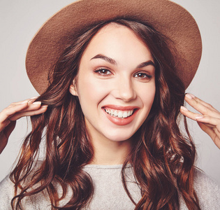 年轻时尚的笑女孩的肖像在灰色的休闲夏天的衣服棕色帽子与自然妆隔离的灰色背景。看相机