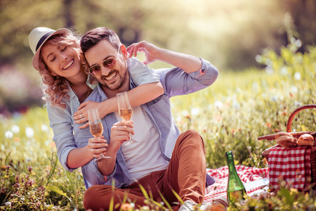 快乐的情侣在一个阳光明媚的日子在野餐时互相微笑。人, 爱, 幸福和自然概念