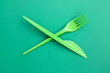 一次性塑料餐具绿色。塑料叉和刀位于绿色背景表面上