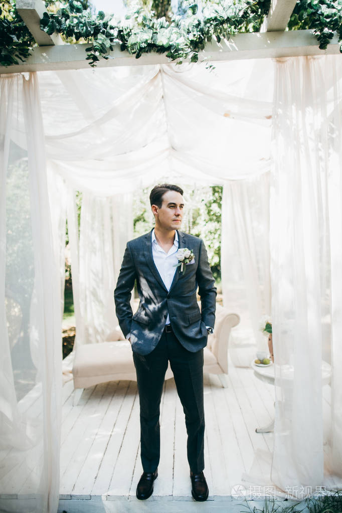 英俊的年轻新郎在夏天的房子摆造型