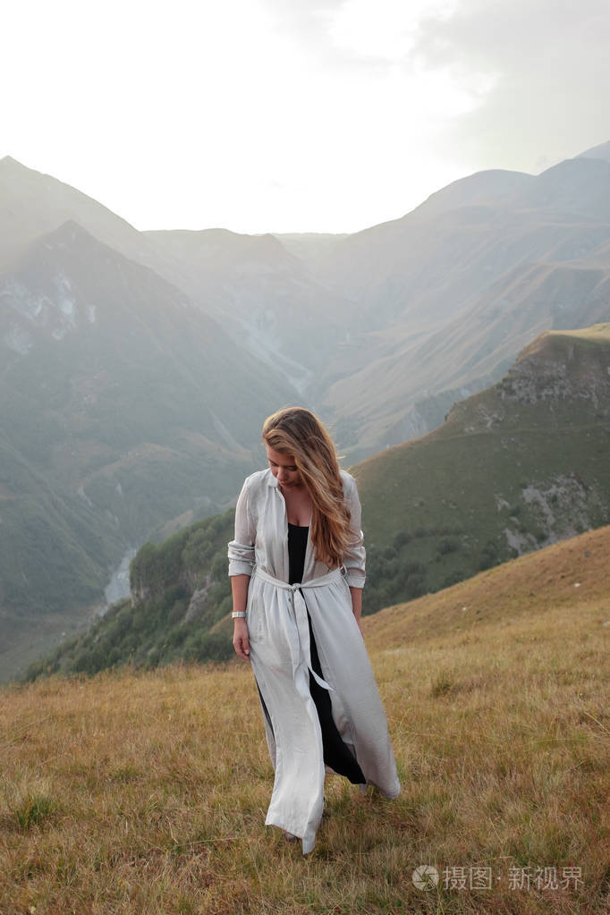 美丽的年轻女子穿着长裙站在山的山谷里