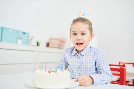 兴奋的小女孩与生日蛋糕坐在幼儿园的桌子上