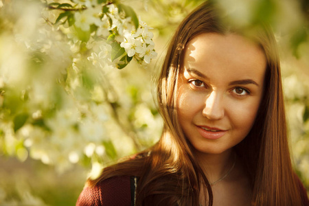 在一棵盛开的苹果树附近有干净皮肤的年轻妇女。春天公园里的女孩肖像