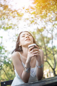 手持咖啡杯的年轻女子坐在户外享受大自然