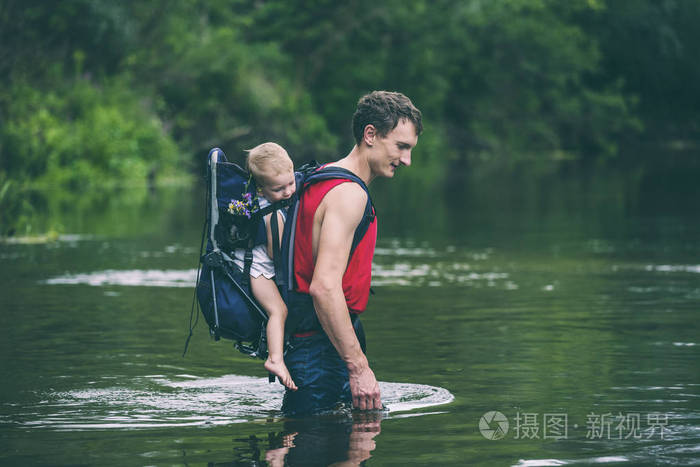 一个带着孩子的男人过河.父亲把儿子扛在背包里.洪水救援.