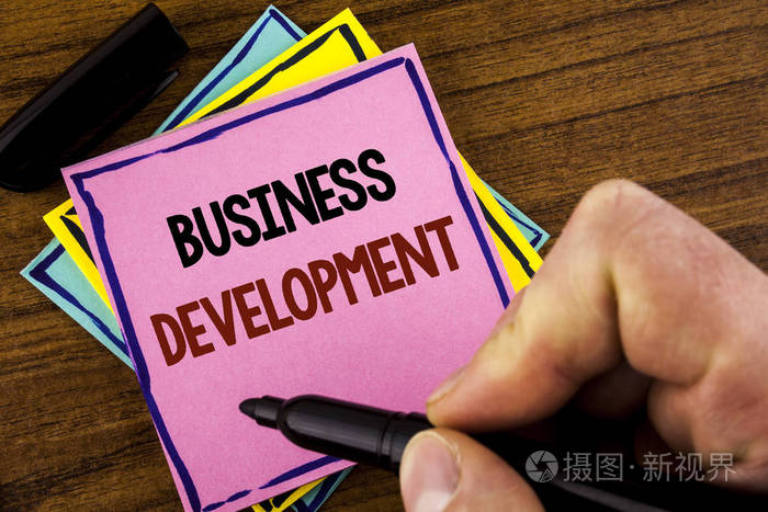 文字书写业务发展。开发和实施组织增长机会的商业概念粉红色粘滞便笺纸在木质背景上持有标记