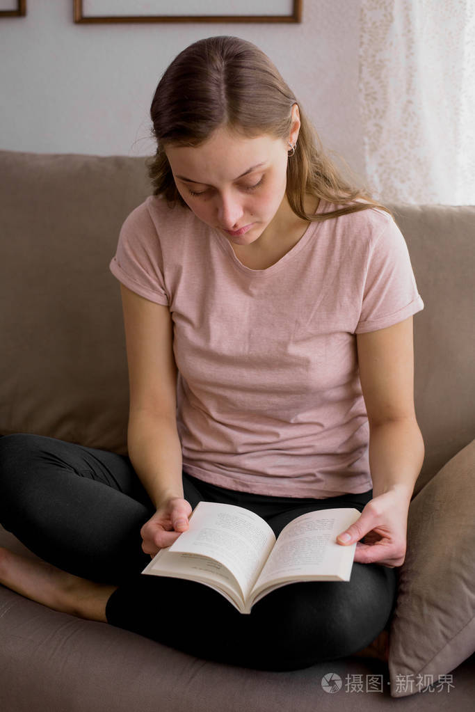 坐在沙发上的有吸引力的年轻妇女的画像在家和读一本书