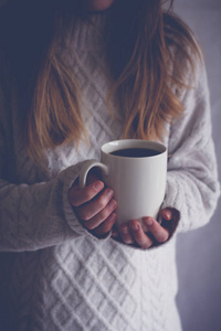 一个金发女孩的腹部, 在室内和阴影中捧起一只白色的杯子人手捧起五颜