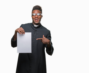年轻的非洲裔美国牧师男子在孤立的背景持有空白纸非常高兴地指着手和手指