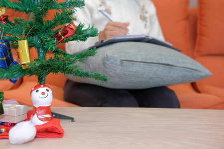 妇女穿着奶油羊毛衫写笔记在笔记本电脑在家里礼品礼物盒圣诞树上表。圣诞新年庆典