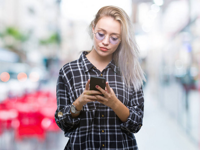 年轻的金发女子发短信发送消息使用智能手机在孤立的背景与自信的表情在聪明的脸思考严重