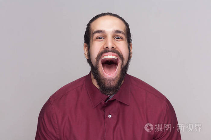 滑稽惊奇的人与黑头发和胡子在红色衬衣站立和看在照相机与大张开的嘴