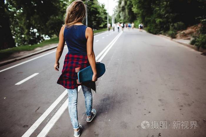 背上的金发女郎背着滑板走在路上照片-正版商用图片071653-摄图新视界