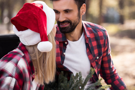 美丽的幸福夫妇在圣诞老人的帽子看着对方在森林里