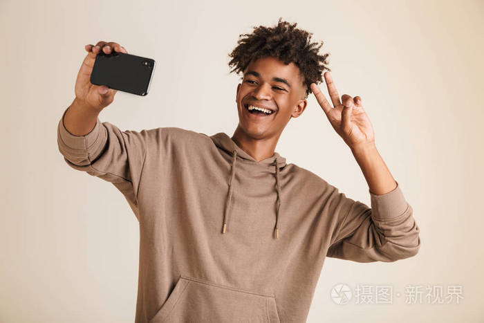 一个欢快的年轻黑人美国男子的照片身着帽衫采取自拍孤立, 而显示和平