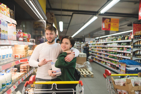 快乐的年轻夫妇摆在超市里, 手里拿着牛奶。超市的家庭购物