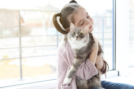 在家窗口附近猫的可爱的小女孩