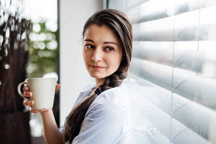 窗边的女人拿着一杯咖啡。