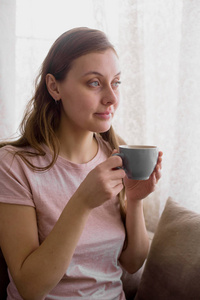 早晨坐在沙发上的漂亮女人喝着茶