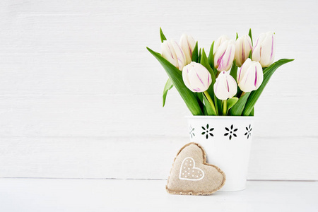 白色的郁金香花束在白色花瓶装饰用纺织品心脏。情人节的概念。复制空间