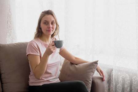 早晨坐在沙发上的漂亮女人喝着茶