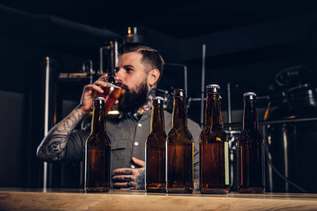 照片与工艺啤酒瓶的前景和胡子男性饮酒的背景
