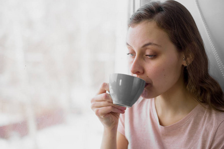 早晨坐在窗边的漂亮女人喝茶