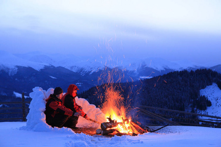 男人取暖火炉旁年轻的夫妇在阳光明媚的日子里, 在森林里露营的篝火旁