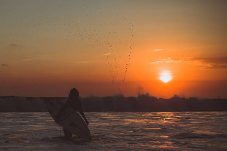 冲女剪影与冲浪板在海 , 日落反射在水和飞溅的水滴